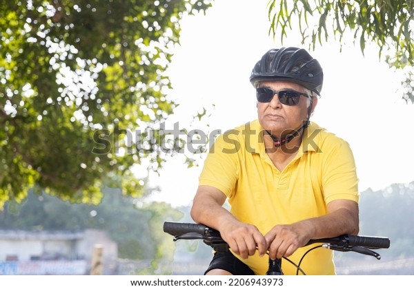 Thoughtful senior man in protective sportswear\
leaning on bicycle handlebar\
outdoors