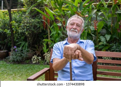 Thoughtful Senior Old Caucasian Man Holding Cane Sitting On Bench In Garden