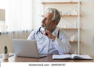 Thoughtful Senior Older Male General Practitioner Looking In Distance, Distracted From Work In Hospital. Pensive Middle Aged Doctor Thinking Of Medical Problem Solution Or Disease Treatment Indoors.