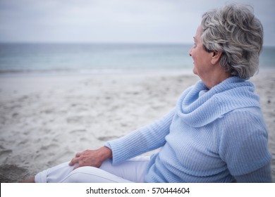 Thoughtful senior woman sitting on beach on a sunny day - Powered by Shutterstock