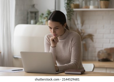 Thoughtful serious freelance worker woman working from home kitchen, using laptop, thinking over email letter, online project. Focused student girl studying on internet sitting at computer on table - Shutterstock ID 2144529681