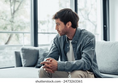 Thoughtful serious man sitting on sofa alone at home, lost in thoughts, thinking about problem solving, feeling lonely, making important decision, having psychological problem, side view - Powered by Shutterstock