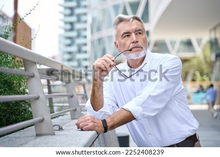 Thoughtful serious older senior business man thinking or future goals standing outdoors. Pensive worried old businessman lost in thoughts, making decision, having dilemma or question in city.