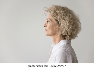 Thoughtful serious pretty blonde mature woman standing at white studio background, looking away in deep thoughts. Beautiful senior model wir curly fair hair side portrait - Powered by Shutterstock