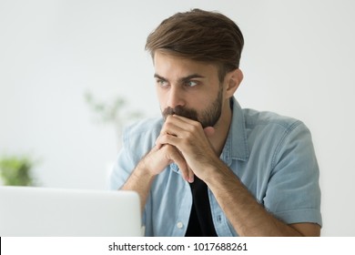 Thoughtful serious young man lost in thoughts in front of laptop, focused businessman or absent-minded student thinking of problem solution, worried puzzled manager pondering question at work