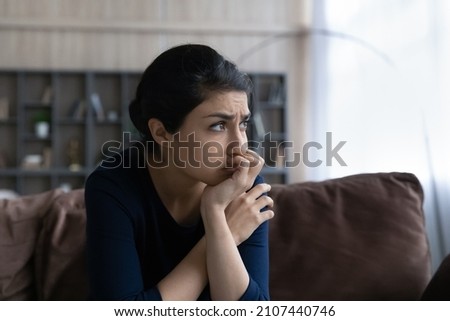 Thoughtful stressed young Indian ethnic woman looking in distance, considering psychological problem solution, suffering from depression or feeling doubtful making difficult decision at home.