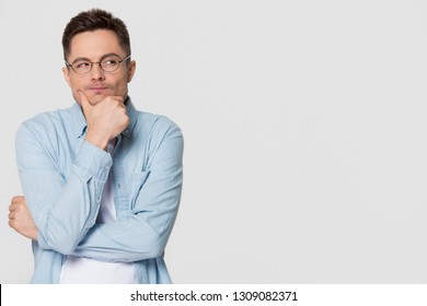 Thoughtful suspicious young man looking aside at copy space feeling skeptic doubtful, distrustful sly cunning guy thinking holding hand on chin isolated on grey white studio background