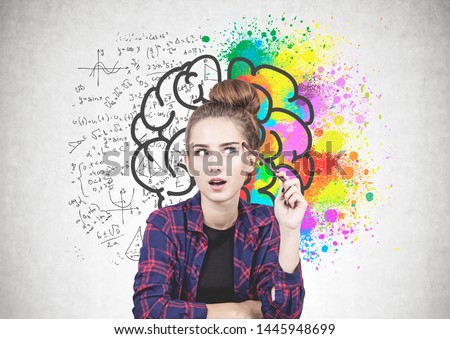 Thoughtful teen girl in casual clothes sitting near concrete wall with colorful brain sketch drawn on it. Concept of brainstorming.