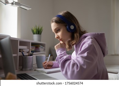 Thoughtful teenage girl in wireless headphones sit at desk at home handwrite in notebook do prepare homework using laptop, smart focused teenager study on computer online, education concept