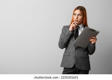 Thoughtful transgender secretary with clipboard on grey background