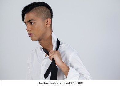 Thoughtful transgender woman holding tie while standing against white background