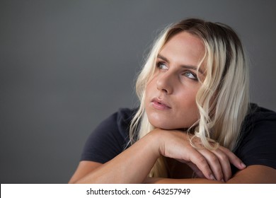 Thoughtful transgender woman leaning on chair over gray background