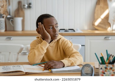 Thoughtful unconcentrated Black schoolboy look to side doing homework sits at table with textbooks. Unmotivated pupil child looks out the window, lazy. Children and education, homeschooling concept - Powered by Shutterstock