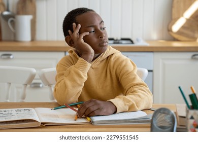 Thoughtful unconcentrated Black schoolboy look to side doing homework sits at table with textbooks. Unmotivated pupil child looks out the window, lazy. Children and education, homeschooling concept - Powered by Shutterstock