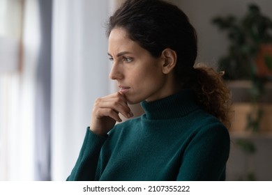 Thoughtful unhappy jealous young hispanic latin woman touching chin, standing near window, considering problem solution or feeling stressed of difficult life situation, bad mood depression concept. - Powered by Shutterstock