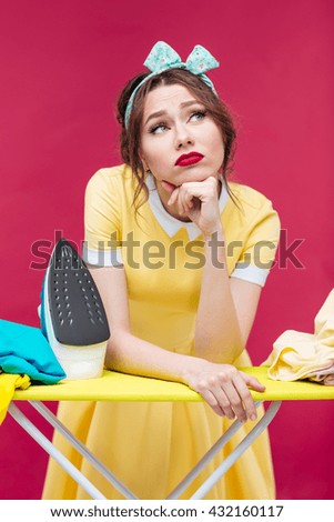 Thoughtful unhappy pinup girl ironing clothes over pink background