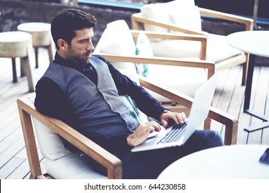 Thoughtful Wealthy Businessman Work On-line On Net-book While Sits At Modern Restaurant Terrace, Young Intelligent Rich Man Connecting To Wireless Via Laptop Computer During Work Break In Coffee Shop