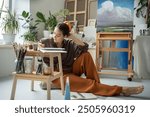 Thoughtful woman artist experience inspiration crisis, pondering over drawing in album sits on floor in art studio, thinks about ideas. Pensive girl painter in creative workshop sketching illustration