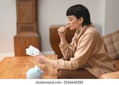 A thoughtful woman contemplates finances while reviewing documents in a cozy living room during the afternoon - Powered by Shutterstock