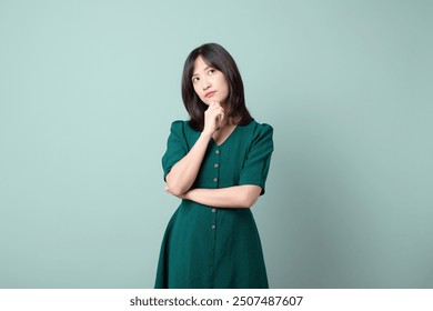 A thoughtful woman in green dress poses with her hand on her chin, expressing curiosity.  - Powered by Shutterstock