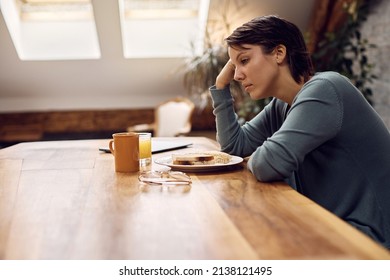 Thoughtful woman having no appetite while sitting at dining table at home. 
