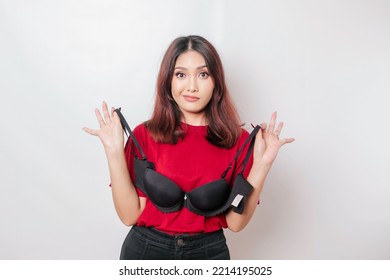 A thoughtful woman is holding a bra against a white background. Concept of Breast cancer awareness and international no bra day celebration