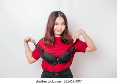 A thoughtful woman is holding a bra against a white background. Concept of Breast cancer awareness and international no bra day celebration
