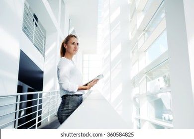 Thoughtful Woman Holding Digital Tablet And Looks Into The Window After Business Meeting With Partners, Young Successful Female Financier Ponders Over The Future Of Company During Work Break In Office