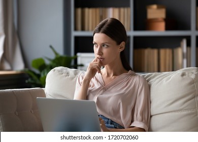 Thoughtful woman holding laptop on laps, pondering ideas or tasks, sitting on couch at home, dreamy young female touching chin and looking in distance, lost in thoughts, waiting for message