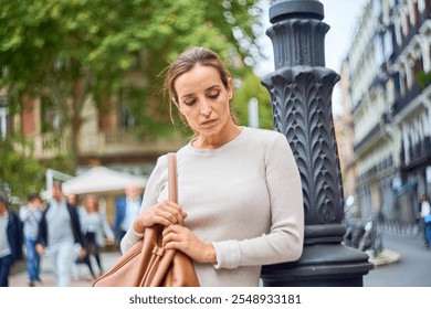 Thoughtful woman leaning against a lamppost in the city - Powered by Shutterstock