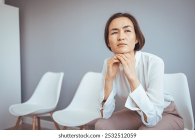 A thoughtful woman in professional attire sits in a modern waiting room, exuding contemplation and focus. The serene environment highlights a calm and introspective atmosphere. - Powered by Shutterstock