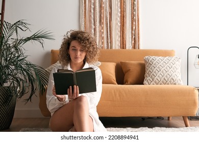 Thoughtful woman reading book in living room - Shutterstock ID 2208894941