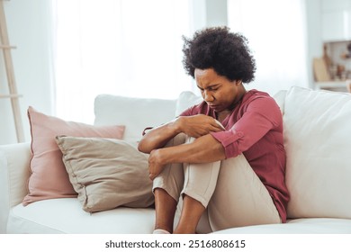 A thoughtful woman sits on a couch at home, looking stressed and pensive. The cozy setting highlights feelings of concern and introspection. - Powered by Shutterstock