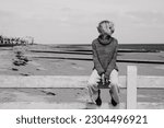 Thoughtful woman sits on the ocean. Middle age woman. Crisis, depression concept. Black and white photo.