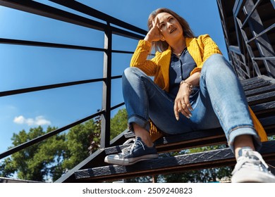 thoughtful woman sitting alone on outdoor stairs. - Powered by Shutterstock