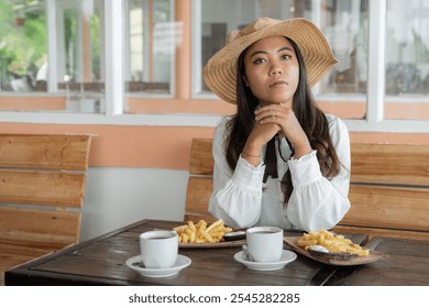 A thoughtful woman in a straw hat and elegant blouse enjoys coffee and fries at a cozy cafe, creating a relaxed and stylish atmosphere - Powered by Shutterstock