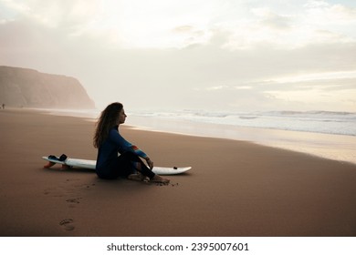 Thoughtful woman with surfboard sitting at beach स्टॉक फ़ोटो