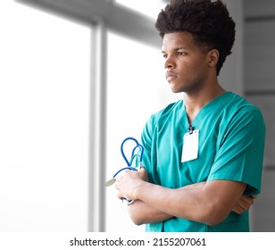 Thoughtful young african american doctor standing by window looking away arms crossed. Portrait male doctor holds stethoscope seriously thinking, pondering. Professional medical occupation lifestyle. - Powered by Shutterstock