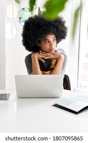 Thoughtful young African American female student with Afro hair using laptop looking through window thinking of inspiration ideas sitting at cafe table alone indoor. Social distancing remote work.
