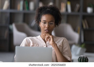 Thoughtful young African American woman in glasses look at laptop screen work online at home office. Pensive ethnic female use computer distant think ponder of problem solution. Technology concept. - Powered by Shutterstock