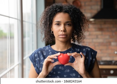 Thoughtful young african ethnicity female volunteer holding heart in hands. showing support to vulnerable people. Kind millennial biracial woman feeling thankful, gratitude or empathy concept.