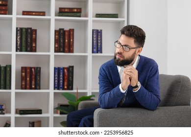Thoughtful young bearded man in armchair at home - Shutterstock ID 2253956825