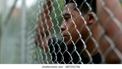 Thoughtful Young Black Man Leaning On Metal Fence At Basketball Court