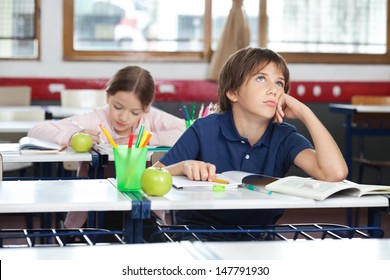 Thoughtful young boy looking up with girl in background at classroom - Powered by Shutterstock