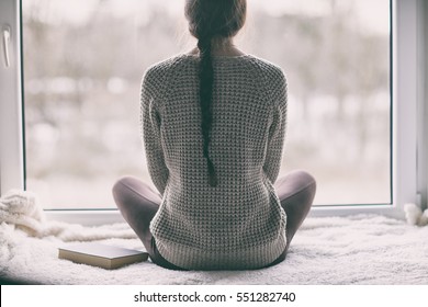 Pensativo jovem morena mulher com livro olhando através do janela, embaçada inverno forrest paisagem fora