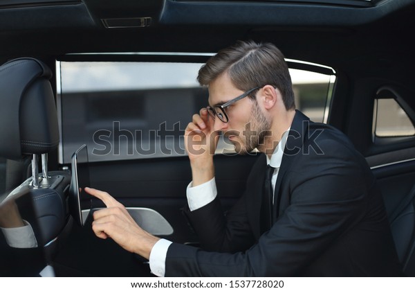 Thoughtful young businessman sitting in the luxe\
car and using his\
tablet.