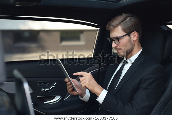 Thoughtful young businessman sitting in the luxe
car and using his
tablet.