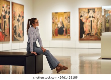 Thoughtful young Caucasian woman wearing glasses and looking at exhibition. Concept of Museum Day. - Powered by Shutterstock