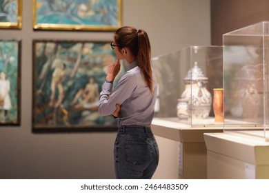 Thoughtful young Caucasian woman wearing glasses and looking at exhibition. Concept of Museum Day. - Powered by Shutterstock