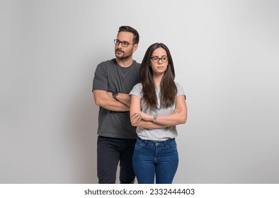 Thoughtful young couple with arms crossed standing confidently against isolated background. Contemplative man and woman wearing eyeglasses and casuals looking away seriously - Powered by Shutterstock